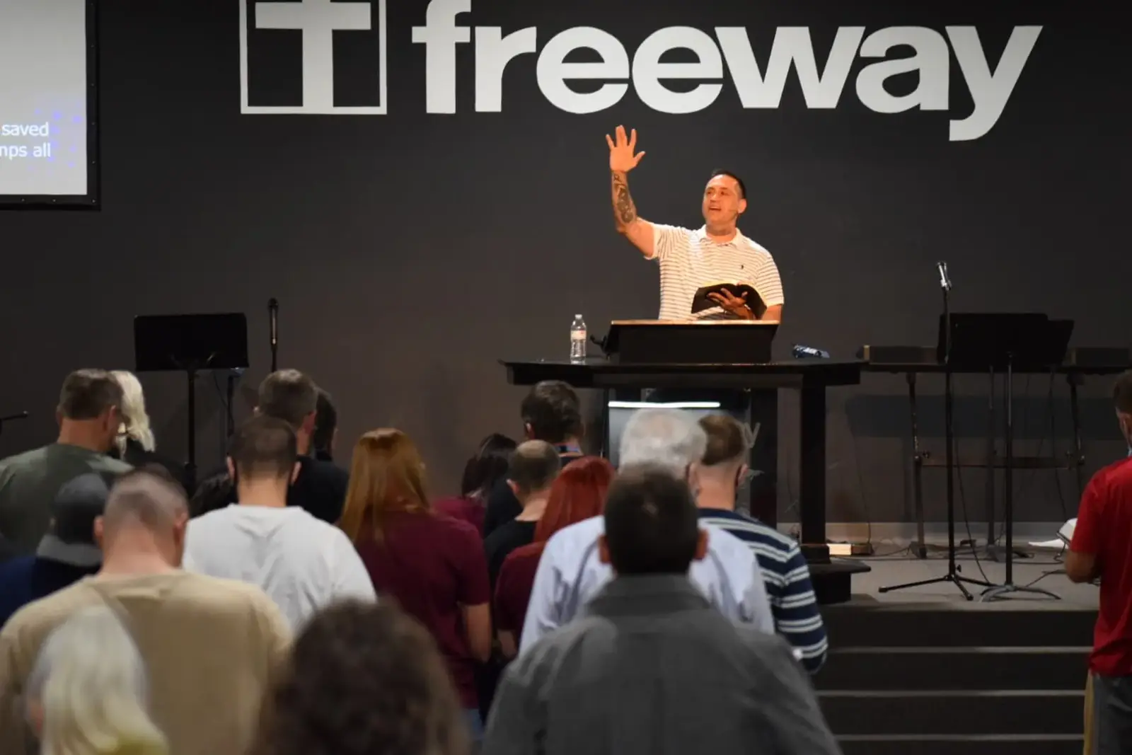 A Freeway preacher with his hand raised before a full room
